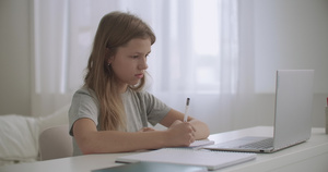 少女在家里很远的地方学习看笔记本电脑的屏幕和写作练习本16秒视频