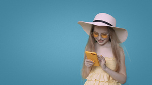 穿着黄色衣服的女孩在蓝背景前浏览智能手机24秒视频