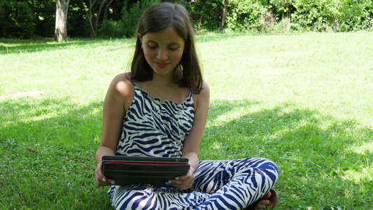 美丽的笑着微笑的少女在户外用平板电脑视频