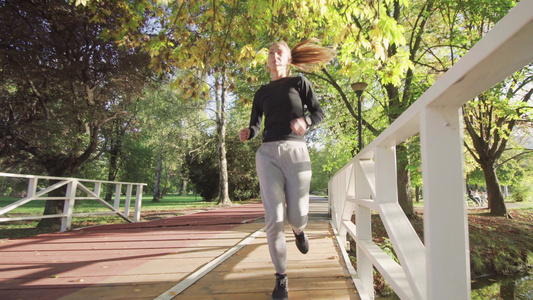 健身女孩在公园的木桥上在全天候的合成轨道表面跑来跑去视频