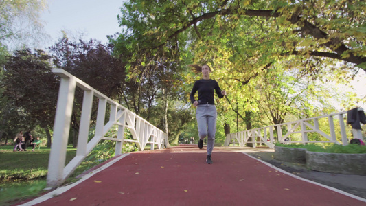 健身女孩在公园的木桥上在全天候的合成轨道表面跑来跑去视频