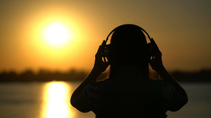 在日落时用耳机收听音乐的女人15秒视频
