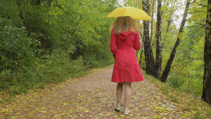 下雨天身穿红色斗篷打着黄色雨伞的年轻苗条女子20秒视频