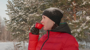 穿着红冬夹克的笑着女人在寒冷的一天在雪林里喝茶29秒视频