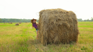 戴着帽子的女牛仔在村庄的收割场从干草堆里窥视戴着帽子11秒视频