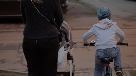 大男孩骑自行车在街上与两个孩子的母亲在一起视频