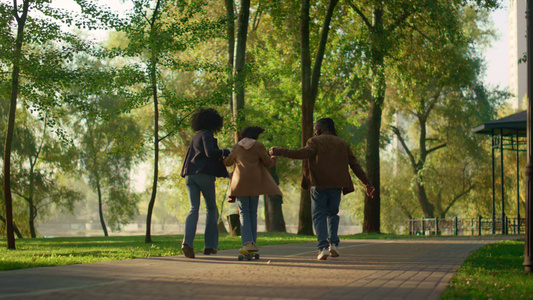 在阳光明媚的秋天公园镜中女孩骑着长板牵着父母的手视频