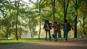父母抱着孩子在阳光明媚的绿色公园玩滑板24秒视频