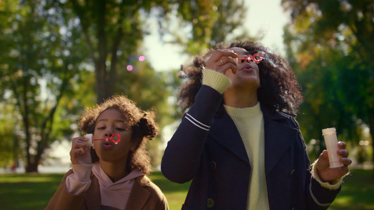 父母和孩子一起在阳光明媚的绿色公园里吹肥皂泡泡视频