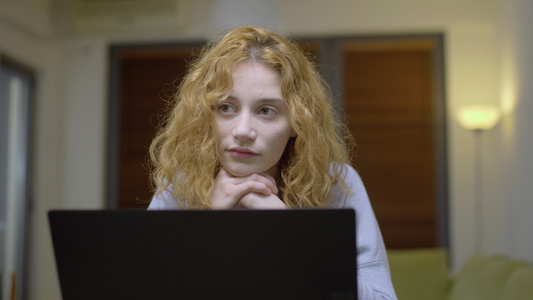 可爱的女孩坐在客厅的桌子上在笔记本电脑前把头发放在视频