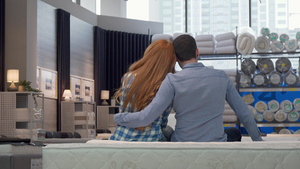 坐在家具店新床铺的一对夫妇抱抱的后视镜头8秒视频