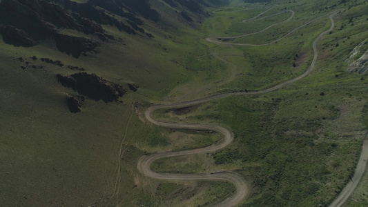 在夏日的山区飞越弯曲的蛇形道路鸟瞰图无人机向后飞行视频