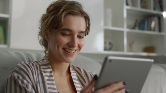 肖像微笑的女人在家里拿着平板电脑阅读好消息视频