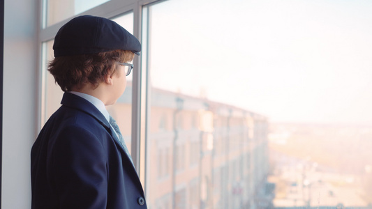 身穿商业西装领带和帽子的年轻男孩从商务办公室的窗口视频