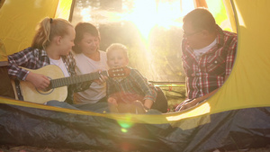 幸福的家庭在阳光背景下的野营帐篷里用吉他唱歌旅游家庭18秒视频