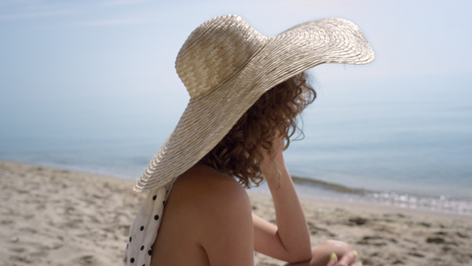 诱人的女人坐在沙滩上戴着宽边帽视频