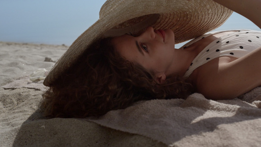 欢快的微笑女孩从躺在沙滩上的宽边帽中望去视频