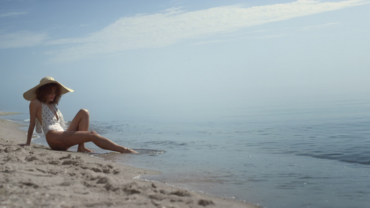 放松的女人坐在沙滩上用沙子在海浪中洗腿视频