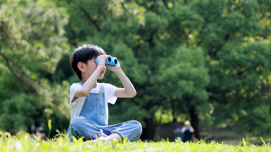 小男孩坐在草地上拿望远镜望向远方视频