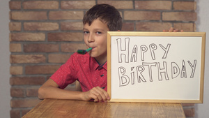 坐在桌边的小孩拿着翻页图在红砖墙上写着生日快乐9秒视频