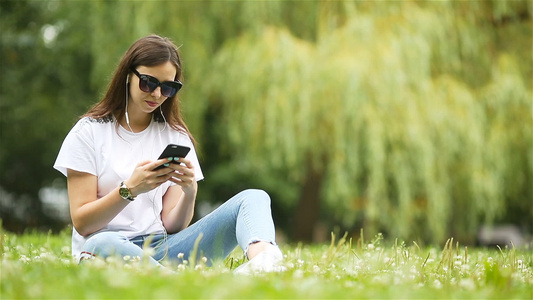 可爱女人坐在公园里时正在看手机短信的短信笑声视频