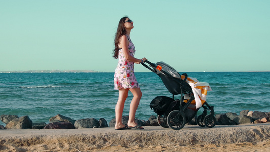 长头发的年轻妈妈在海边推着婴儿车散步视频