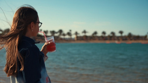 长头发的小女孩在海边喝果汁享受美丽风景11秒视频