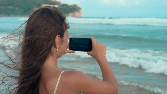 在海边享受风景的快乐女孩拿着手机拍照视频