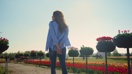 带着相机在阳光下的夏日花卉公园散步的轻松女孩的背影视频