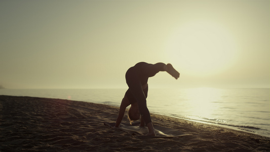 日出时练习瑜伽的女运动员站在海滩上视频