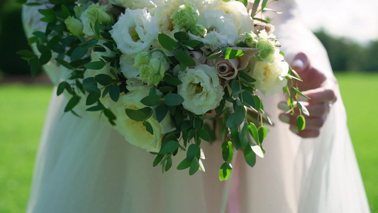 穿着结婚礼服的年轻新娘在公园里拿着花束花白色豪华礼服视频