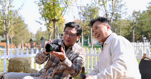 两个老年男人坐在房车露营院子里看数码相机20秒视频