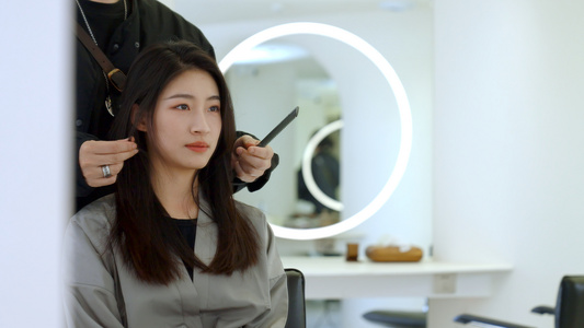 女顾客通过镜子看发型师给自己做造型视频