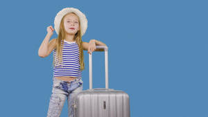 旅行的女孩带着手提箱打招呼在工作室的蓝色背景上打着16秒视频