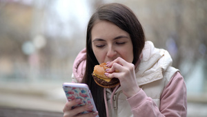快乐的女人吃汉堡在街上用智能手机18秒视频