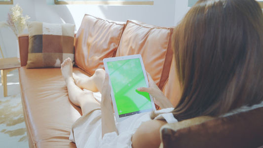 4K女性沙发上划平板电脑绿幕素材视频