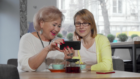 成熟女性和她的老母亲在咖啡馆一起使用智能手机视频