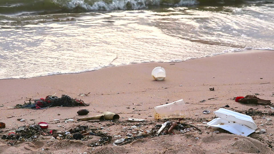 海边日落海滩上有塑料和废物海浪将它们吹入海中视频