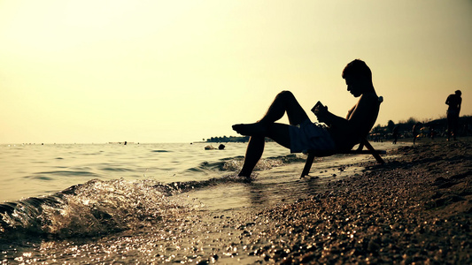 坐在椅子上的人在海滩日落日出电影Dof上读书视频