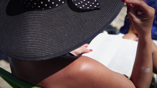 戴着帽子的年轻性感女人在海滩上读书视频