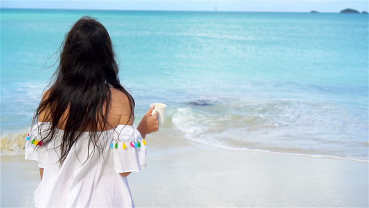 有热咖啡的年轻女子享受海滩风景美丽的女孩在慢动作视频视频