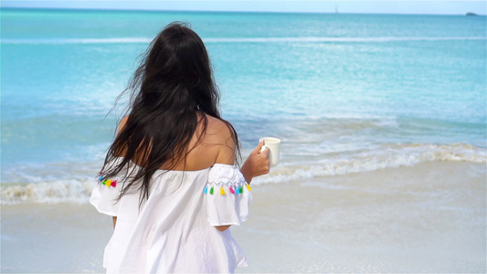 在白色热带沙滩上喝着热饮的年轻女子慢动作女孩享受美丽视频