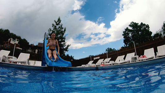 穿比基尼的少女从塑料幻灯片滑下来冲进游泳池慢动作视频