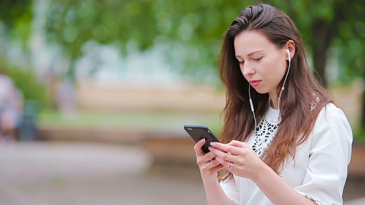 年轻的白种女人在公园里用她的智能手机在户外发送信息视频