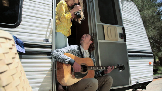 年轻女子在大篷车外弹吉他时拍摄男友视频