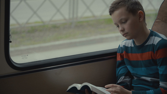 一名年轻男中学生搭乘公共汽车穿过城市阅读一本书的近视频