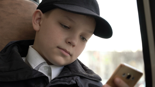 一名男孩在城市中搭乘公交车旅行的近距离拍摄他使用智能手机视频