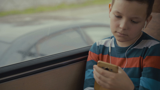 一个小男孩乘公共汽车穿越城市的特写镜头他在智能手机视频