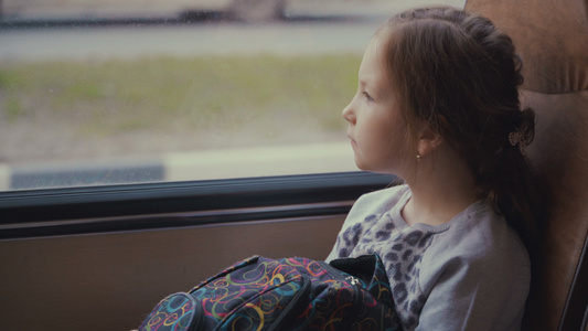 年轻美丽的女孩乘着学校包在移动校车的客车上向窗外看视频
