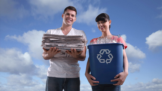 一对夫妇在田野里拿着回收箱和一堆报纸视频